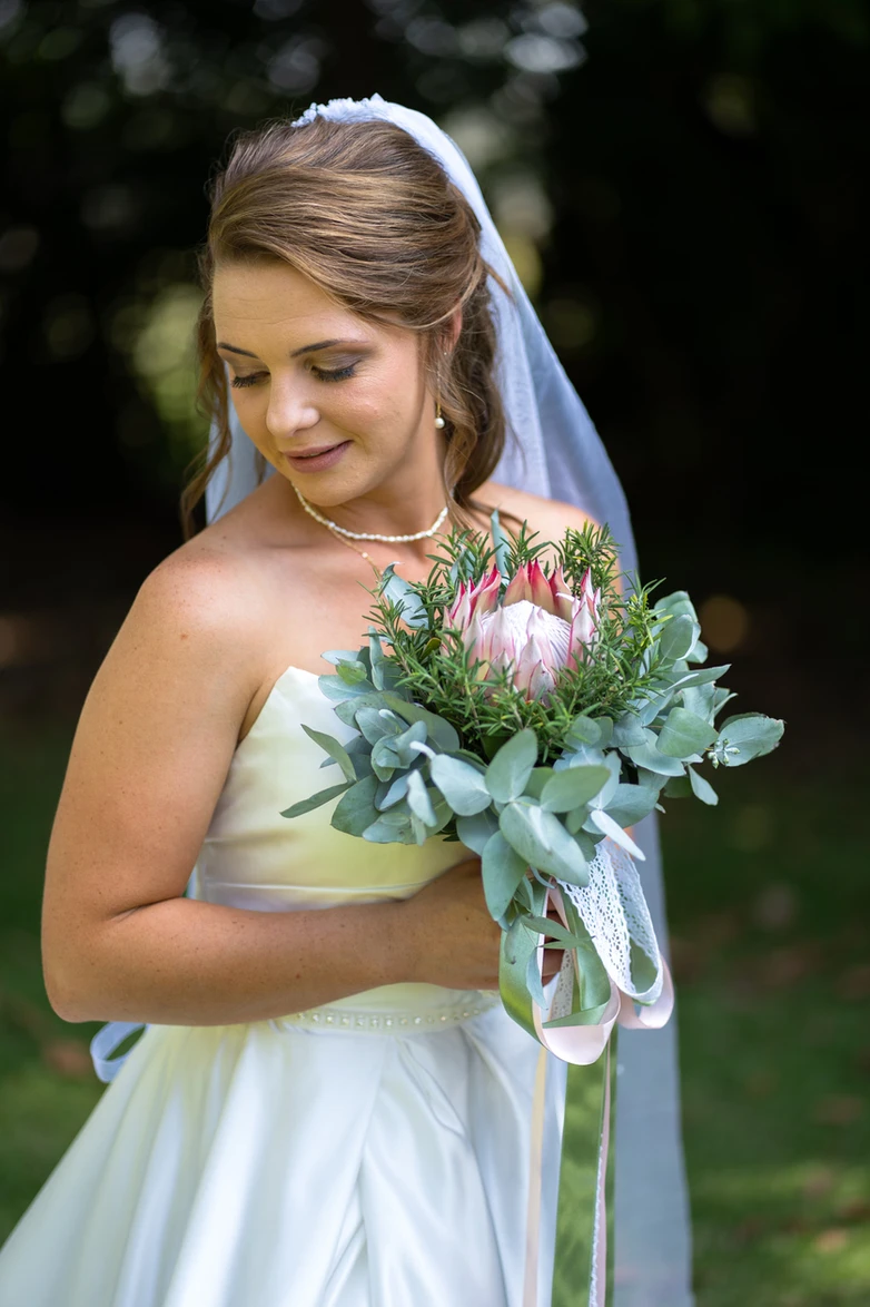 Bride smiling down at her protea bouquet